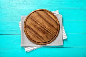 Frame of round cutting board on a striped and gray tablecloth on blue wooden background. Top view and place for text photo