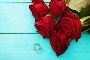Wedding rings and red roses. Wedding bouquet on blue wooden background. Selective focus. Copy space and mock up photo