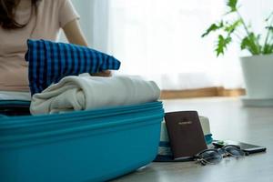 primer plano de una joven que dobla ropa y artículos como sombreros, anteojos y pasaportes. poner en una maleta, prepararse para descansar en un viaje foto