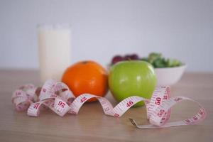 concéntrese en la cinta métrica: comida saludable con ensalada de verduras, naranja, manzana y leche. concepto de dieta foto