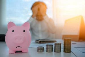 Piggy bank sad with pile coins focus. blur man stressed with Debt and expenses problems, no money to pay, checks, credit card, Broke, mortgage, loan, bankruptcy photo