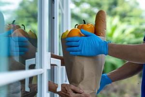 el repartidor envía bolsas de comida a los clientes frente a la casa durante la epidemia de covid-19. El remitente usa guantes protectores. orden en línea y servicio de entrega rápida foto