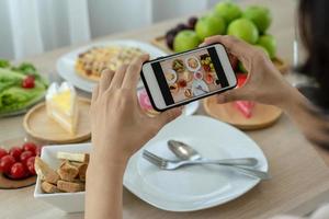 las mujeres usan teléfonos móviles para tomar fotografías de alimentos o grabar videos en vivo en aplicaciones de redes sociales. la comida para la cena se ve apetitosa. fotografiar y tomar una foto para revisar los conceptos de comida