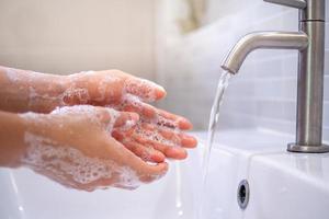 A close up of a young woman's hand washing hands with soap gel in the bathroom sink hand cleaning to prevent the spread of the covid19 virus. Health care concept
