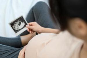 A pregnant woman is looking at an ultrasound photo of fetus. Mother gently touches the baby on stomach.Women are pregnant for 30 weeks. first love in belly and Last term pregnancy