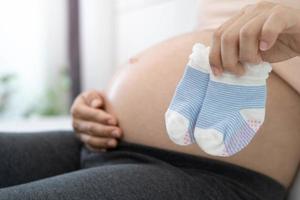 una mujer embarazada de 8 meses está feliz de preparar calcetines para el bebé. buena madre o mama foto