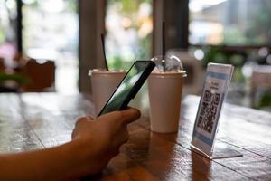 los hombres usan teléfonos para escanear un código qr para seleccionar un menú o escanear para recibir un descuento o pagar comida y bebida dentro de un café. usar el teléfono para transferir dinero o pagar en línea sin concepto de efectivo. foto