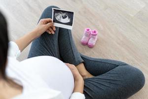 una mujer embarazada está mirando una foto de ultrasonido del feto. la madre toca suavemente al bebé en el estómago. las mujeres están embarazadas durante 30 semanas. primer amor en el vientre y último embarazo