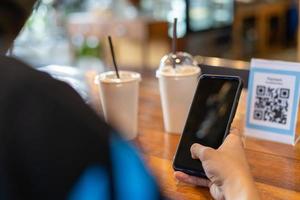 los hombres usan teléfonos para escanear un código qr para seleccionar un menú o escanear para recibir un descuento o pagar comida y bebida dentro de un café. usar el teléfono para transferir dinero o pagar en línea sin concepto de efectivo. foto