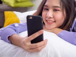 The girl smiled and enjoyed a video conference with a friend or boyfriend using a mobile camera while lying in bed at home. stay home and happy photo