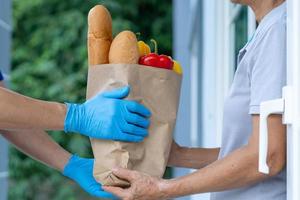el repartidor envía bolsas de comida a los clientes frente a la casa durante la epidemia de covid-19. El remitente usa guantes protectores. orden en línea y servicio de entrega rápida foto
