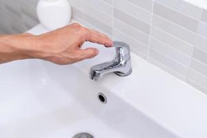 el grifo del baño con agua corriente. el hombre sigue cerrando el agua para ahorrar energía y proteger el medio ambiente. concepto de ahorro de agua foto