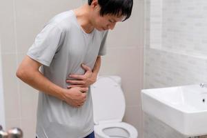 diarrea, dolor abdominal, concepto de estreñimiento. los hombres tienen contracción y dolor de estómago. hombre sosteniendo papel higiénico en el baño. foto
