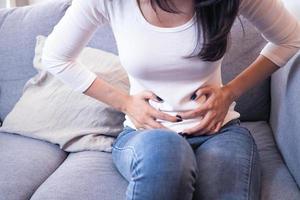 la mujer enferma tiene dolor de estómago severo sentada en el sofá. concepto de gastritis o calambres menstruales foto