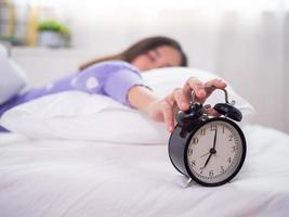 la mujer dormida durmiendo en la cama, usando la mano para presionar el despertador por la mañana. buenos días en un día perezoso foto