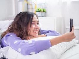 la niña sonrió y disfrutó de una videoconferencia con un amigo o novio usando una cámara móvil mientras estaba acostada en la cama en casa. quédate en casa y feliz foto