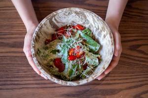 Ensalada de verduras en un cuenco de madera. La mano de la mujer muestra una ensalada eligiendo alimentos saludables para el cuerpo, comiendo verduras y frutas. Buenas pautas para bajar de peso.