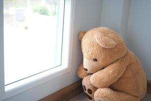 Child concept of sorrow. Teddy bear sitting leaning against the wall of the house alone, look sad and disappointed. photo