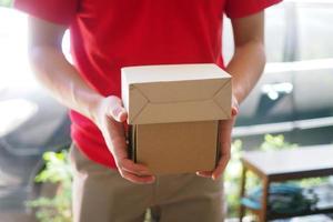 el cargador del traje azul sostiene una caja marrón frente a la casa del cliente. envío gratuito para compras en línea y entrega urgente foto