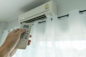 la mano del hombre fuera del acondicionador de aire sujetando el control remoto al sistema de refrigeración después de que no haya nadie en la habitación. Ahorre electricidad, ahorre energía y proteja el medio ambiente. foto