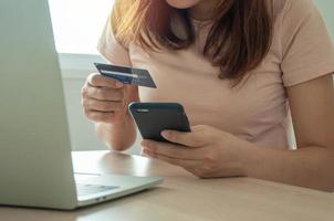 una mujer joven usa una tarjeta de crédito para comprar pagos en línea en una aplicación de computadora portátil o en un sitio web. concepto de comercio electrónico y compras en línea. quédate en casa y compra productos en línea.