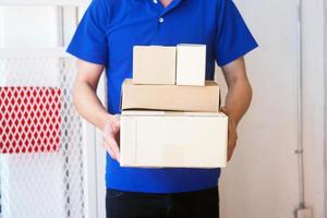 el cargador del traje azul sostiene una caja marrón frente a la casa del cliente. envío gratuito para compras en línea y entrega urgente foto