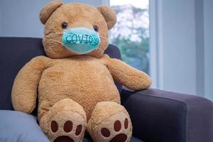 Teddy bears sitting on the sofa in the house with a mask written in Covid-19. The situation of the virus covid19 infection is spreading around the world. photo