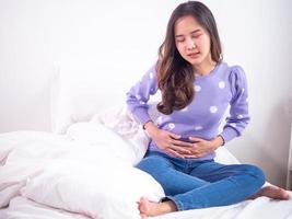las mujeres asiáticas tienen dolor de estómago mientras están sentadas en la cama en el dormitorio después de despertarse. concepto de dolor menstrual foto