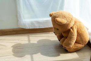 The teddy bear looked sad and disappointed sitting in the corner of the room. The teddy bear seems lonely in a room with sunlight. concept depression in children photo
