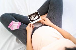 A pregnant woman is looking at an ultrasound photo of fetus. Mother gently touches the baby on stomach.Women are pregnant for 30 weeks. first love in belly and Last term pregnancy