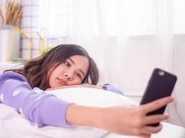 Asian women use mobile phones to watch Korean series and play games in bed. Feeling bored of the same behavior that must be at home to reduce the spread of the virus covid-19. photo