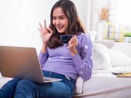 una chica asiática usa una computadora portátil para hablar por videoconferencia en la casa. requiere que los amigos pasen tiempo juntos durante las vacaciones y la distancia social. quédate en casa feliz foto