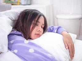 A beautiful Asian woman is sleeping and hugging a pillow in holiday. Lazy woman wake up or wake up late concept photo