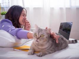 una mujer está jugando con un gato en el dormitorio y tiene una reacción alérgica a la piel. use las manos para cubrirse la boca y estornudar. foto