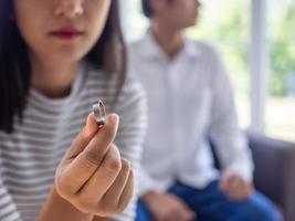 An Asian woman is taking off wedding ring and looks sad. Behind her husband to focuses on family problems and Say goodbye. divorce and love problem concept photo