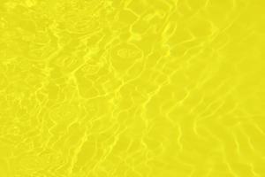 desenfoque borroso transparente color amarillo claro agua tranquila textura superficial con salpicaduras y burbujas. fondo de naturaleza abstracta de moda. ondas de agua a la luz del sol con cáusticos. brillo dorado de acuarela foto