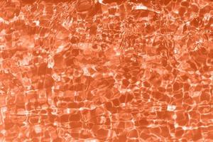 Defocus blurred transparent orange colored clear calm water surface texture with splashes and bubbles. Trendy abstract nature background. Water waves in sunlight with caustics. Orange water shinning photo