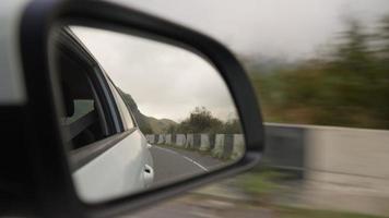 vista desde el interior de un automóvil que conduce a lo largo de la carretera hasta el espejo lateral durante la lluvia. el concepto de vehículos y conductores. nadie. video
