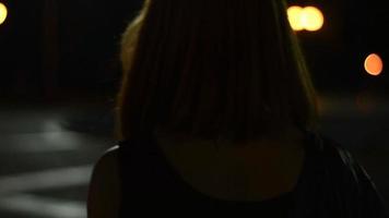 atractiva dama sonriente con el pelo corto camina por la ciudad en la oscuridad de un primer plano de un fondo borroso video