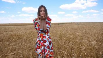 a young girl stands in the field dress and shows in the palms, wheat video