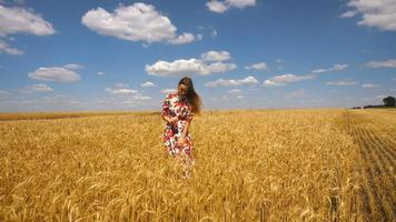 a young girl in a beautiful dress standing in a field with wheat and raises her hands up
