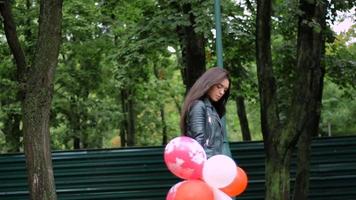 jolie brune aux cheveux épais marche dans la rue avec des boules d'air et regarde la caméra video