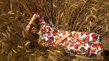 cute pretty girl in a bright dress lies in the wheat field closing face hand and smiles video