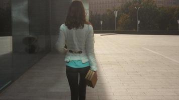 cheerful young brunette student girl walks in the street with books in hands and smiles on camera video