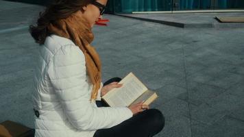 carino giovane brunetta donna nel bicchieri lettura un' libro nel il strada video
