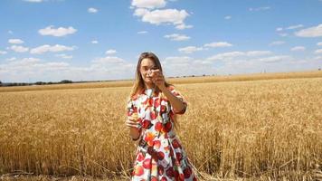 linda garota sorridente em pé em um campo de trigo e infla bolhas de sabão video
