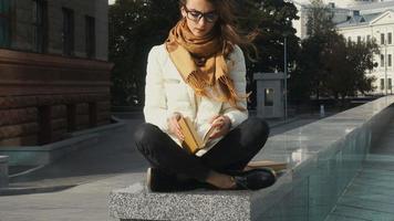 young beautiful girl in glasses reading a book in the street video
