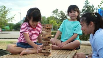 eccitato bambini e mamma giocando jenga Torre di legno bloccare gioco insieme nel il parco. contento famiglia con bambini godendo fine settimana attività insieme. video