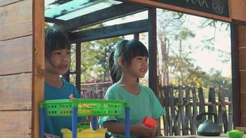 las hermanas felices juegan con comida y juguetes de madera en el patio de recreo al aire libre con su madre. linda chica asiática jugando a vender jugo de frutas en el parque. familia pasando tiempo juntos de vacaciones. video