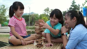 niños emocionados y mamá jugando al juego de bloques de madera de la torre jenga juntos en el parque. familia feliz con niños disfrutando juntos de las actividades de fin de semana. video